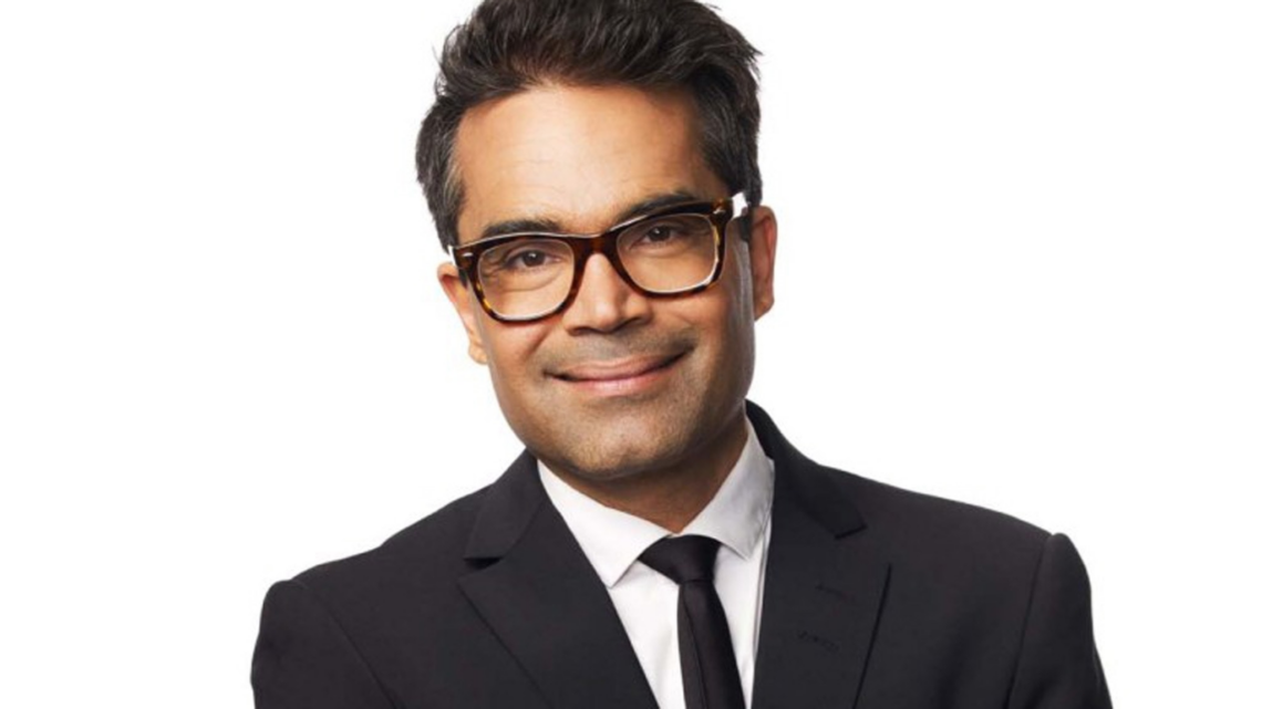 David Batra ler mot kameran i mörk kostym, vit skjorta och glasögon.