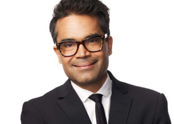 David Batra ler mot kameran i mörk kostym, vit skjorta och glasögon.