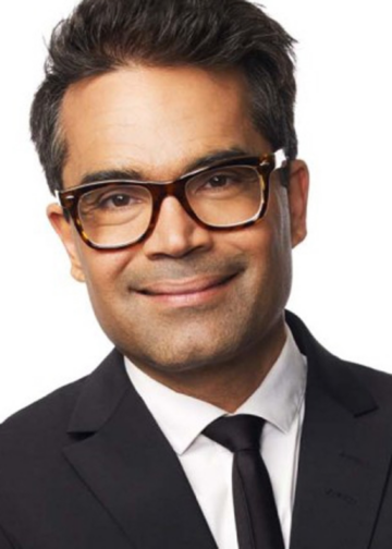 David Batra ler mot kameran i mörk kostym, vit skjorta och glasögon.
